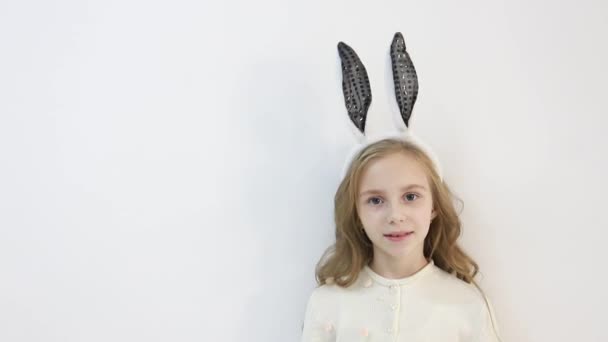 Kleines Mädchen im Mantel, in die Ohren eines Osterhasen gekleidet, ein glückliches Kind wartet auf die Feiertage — Stockvideo