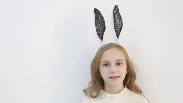 Lächelndes kleines Mädchen im Mantel, gekleidet in die Ohren eines Osterhasen, ein glückliches Kind wartet auf die Feiertage — Stockvideo