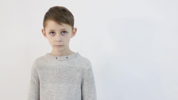 Vtipný malý chlapec na bílém pozadí, smutné dítě se dívá do kamery — Stock video