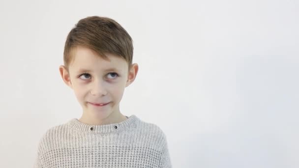 Funny little boy on a white background, sad child looks at the camera — Stock Video