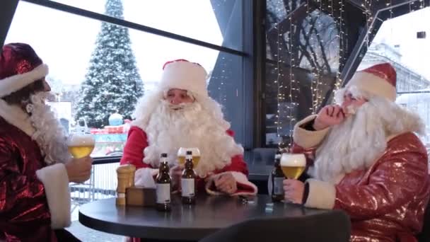 一群圣诞老人祝您圣诞快乐 并喝一杯淡啤酒 三个穿着圣诞老人服装的人在一个圣诞晚会上谈话 — 图库视频影像