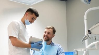 Diş hekimi hasta dişlerinin resimlerini göstermek için bir tablet kullanır. Modern bir diş kliniğinde ağrısız diş tedavisi.