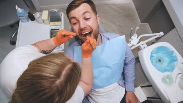 女性歯科医は若い男の歯を扱います 歯科事務所 歯の治療のために口を開けた — ストック動画