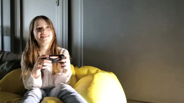 幸せな子供はゲームコンソールで遊んでいる 十代の女の子はゲームジョイスティックを保持している 興味のあるコンピュータモニターを見てください 子供は中毒を演じる — ストック動画
