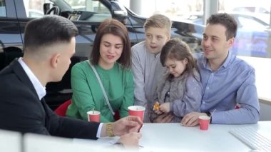 Mutlu aile yeni araba alıyor, araba satıcısı babasıyla tokalaşıyor yeni araba için aileyi tebrik ediyor, 4K video.
