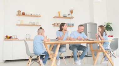 Genç bir aile lezzetli bir şekilde İtalyan pizzası yiyor, masada mutfakta oturuyor, iletişim kuruyor ve eğleniyorlar. Fast food yemeği.