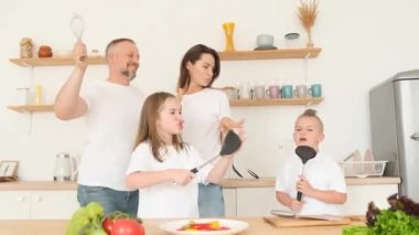 Sanatçı aile mutfakta dans edip şarkı söylüyor, mutlu aile, mikrofon yerine kaşık tutuyorlar, karaokeyi seviyorlar, mutfakta birlikte eğleniyorlar.