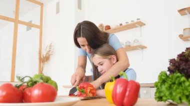 Mutlu ve çekici genç Amerikalı anne ve kız vejetaryen yiyecekler için taze sebze doğradılar. Gülümseyen aile modern mutfakta birlikte yemek hazırlıyor..