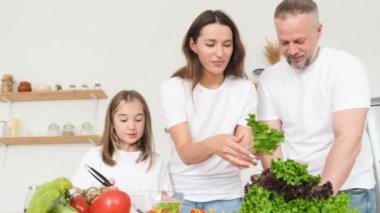 Mutlu aile evdeki mutfakta yemek hazırlıyor. Anne, baba ve kız evde sebze salatası hazırlıyorlar. Sağlıklı Yeme