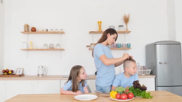 Giovane Madre Intreccia Capelli Dei Suoi Figli Mentre Seduto Cucina — Video Stock