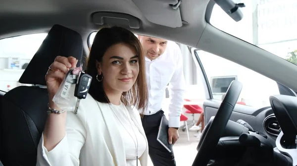 Happy brunette woman showing car key to camera after buying new car. Buying a new car in the showroom