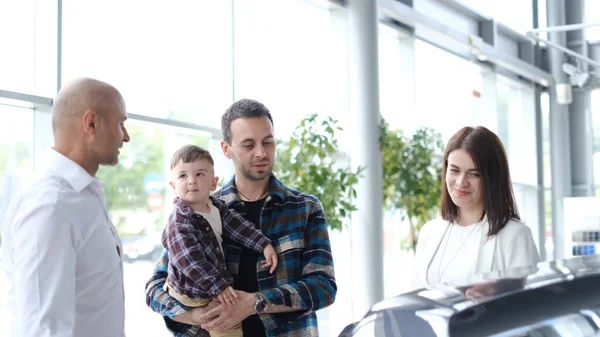 The young family bought a new car. The manager of the car dealership tells customers about the car. Buying a premium family car