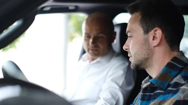 A car salesman sells a car to a young man. The sales manager talks about the new car sitting inside, the buyer chooses a car in the dealership. People and business concept.