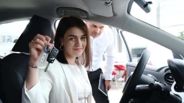 新しい車を購入した後 カメラに車のキーを示す幸せなブルネットの女性 ショールームで新しい車を買う — ストック動画