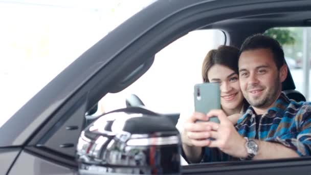 一对恋爱中的夫妇在一家汽车经销店买了一辆新车 他们在车上第一次自拍 满意的丈夫和妻子在新买的车上 — 图库视频影像