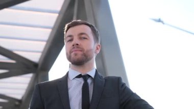 Güneş ışığının arka planında gülümseyen bir işletme yöneticisi. Pozitif genç ofis çalışanı gülümsüyor ve dışarıda kameraya bakıyor. Kamera hareketi. Yavaş çekim