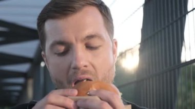 Aç ofis müdürü lezzetli bir hamburger yiyor, yakın çekim. Zararlı sokak yemekleri fast food. 4k video