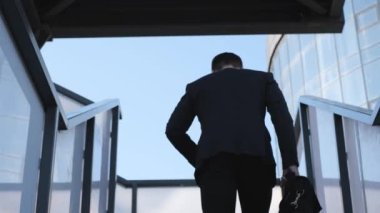 Elinde evrak çantası olan bir iş adamı merdivenleri tırmanıyor, dikiz aynasından. Avrupalı bir adam büro merkezine doğru gidiyor..