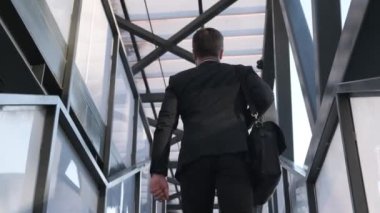 Siyah takım elbiseli genç işadamı merdivenleri tırmanıyor, dikiz aynasından. Bir adam şehirde sokakta yürürken omzunda bir iş çantası tutuyor. Müdür merdivenleri çıkıyor.