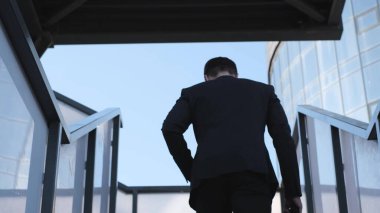 Elinde evrak çantası olan bir iş adamı merdivenleri tırmanıyor, dikiz aynasından. Avrupalı bir adam büro merkezine doğru gidiyor..