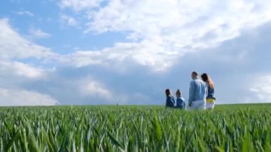 Aile tatili. Genç bir ailenin mutlu hayalleri. Ebeveynlerin oğulları ve kızları yeşil buğday üzerinde yürür. Mutlu aile kavramı. Aile gezisi.