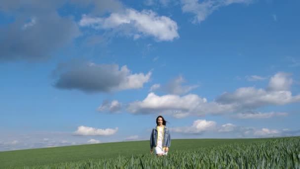 デニムジャケットに身を包んだロングヘアの美少女がひとりで緑の畑を歩いている フリー若いです女の子で緑小麦 — ストック動画