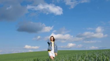 Yeşil buğdaylı mutlu, özgür genç kız. Çekici bir kadın ağır çekimde mutlu bir şekilde yürüyor, buğday başaklarına elleriyle dokunuyor. Doğanın tadını çıkaran kadın