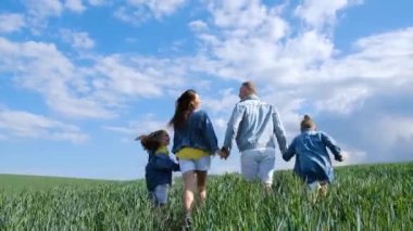 Genç aile koşuyor, el ele tutuşuyor, birlikte mutlular. Anne, baba, kız ve oğul buğday tarlasında koşuyorlar. Özgürlük, mutluluk ve hayaller konsepti