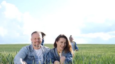 Neşeli aile yeşil buğday tarlasında yürüyor. Ebeveynler çocukları ellerinden tutar. Aile dışarıda koşuyor. Mutlu aile birlikte vakit geçiriyor.