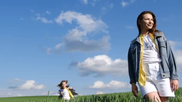 母と娘は若い小麦の緑の分野を歩く 子供たちは緑の新鮮な草の上を走る 幸せな子供たちは田舎の野外で楽しい時間を過ごしています — ストック動画