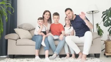 Evdeki kanepede dinlenen mutlu Avrupalı aile, kameraya sevinçle el sallıyor. Aile ve mutluluk kavramı