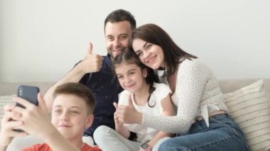 Mutlu ebeveynler ve küçük çocuklar fotoğraf makinesi kullanarak gülüyorlar. Kanepede dinleniyorlar. Aile fotoğrafı.