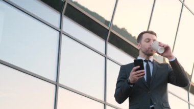 Neşeli genç işadamı smartphone ve içecek fincan holding kullanma.