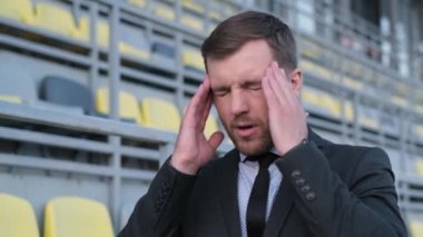 Yorgun bir ofis çalışanı sokağın ortasında duruyor, başı ağrıyor. İş yerinde yorgunluk ve yorgunluk, migren ve depresyon.