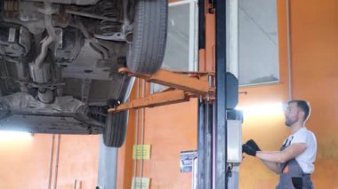 Profesyonel bir araba tamircisi bir araba tamirhanesinde kaldırma makinesinin kralı altında çalışır. Araba servisi, elektrikli arabaların tamiri.