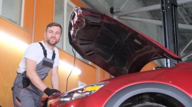 Profesyonel bir mekanik araba servisinin çalışanı arabanın kaputunun altına bakar ve parmağını kaldırır. Tamirci arabayı tamir etti.