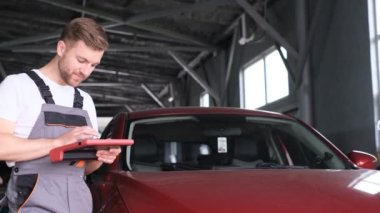 Arabanın bilgisayar kontrolleri. İnceleme, araba elektroniği. Avrupalı araba tamircisinin elinde dijital bir cihaz var. Araba servisinde modern teknolojiler