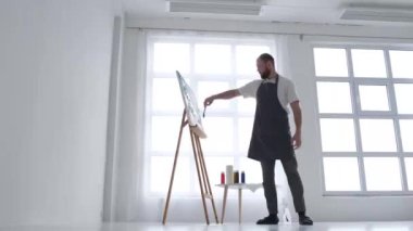 Ressam soyut bir tablo çiziyor, işine odaklanıyor, resim atölyesindeki bir sehpaya resim çiziyor, yaratıcı bir atmosfer yaratıyor.