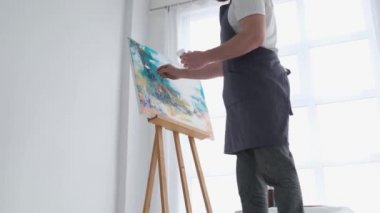 Genç bir erkek sanatçı stüdyoda çalışıyor, büyük beyaz bir tuval üzerinde parlak boya kullanıyor. Soyut sanat sanatçısının modern ve başarılı bir başyapıtı.
