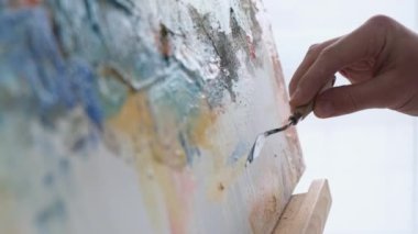 A young male artist works in a studio, he uses bright paint on a large white canvas. A modern and successful masterpiece of drawing by an artist of abstract art