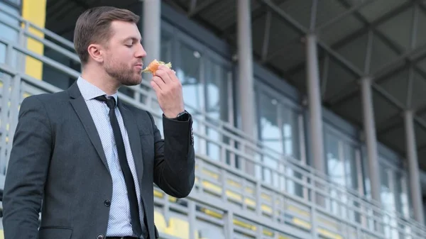 Attractive smiling young businessman in suit eating fast food outdoors, lunch break at office worker. High quality 4k video