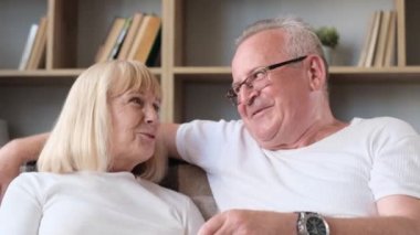 Happy elderly married couple watching TV sitting on sofa, elderly couple eating popcorn and laughing. Grandpa and grandma are happy together in retirement