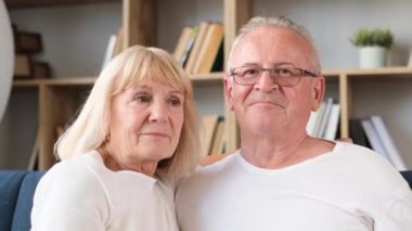 Close-up portrait of retired couple hugging while sitting on couch in living room. Happy couple of grandparents