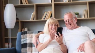 Mutlu Avrupalı emekli çift ellerinde akıllı telefon, komik fotoğraflara bakıp gülüyorlar koltukta otururken, neşeli emekliler ailesi