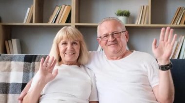 Happy grandparents in love waving hello, watching webcam, they are looking at the camera, talking, waving, hello, goodbye, chatting via online video call