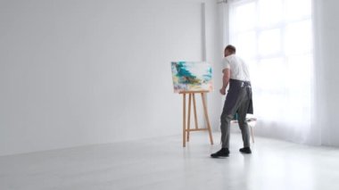 The artist paints an abstract picture, he is focused on work, painting on an easel in his art studio, creative atmosphere