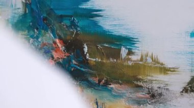 The artist paints an abstract picture, he is focused on work, painting on an easel in his art studio, creative atmosphere