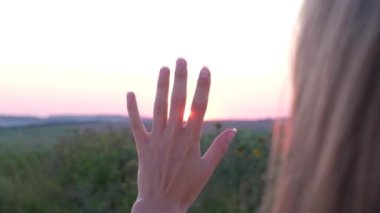 Close up of girls hand at sunset. Sunset between the fingers of a girls hands. A woman with long hair dreamily reaches for the sun. Slow motion