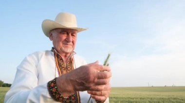 Mavi gökyüzüne karşı işlenmiş gömlekli yaşlı bir dede bir buğday kulağı tutuyor ve başparmağını gösteriyor. Mutlu çiftçi