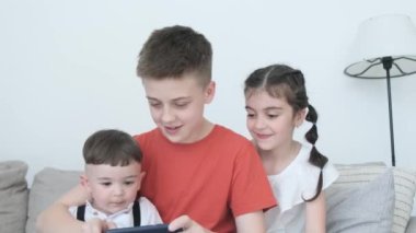 Three cute, cute kids are sitting on the couch in the living room and looking at the phone. Kids and gadgets.